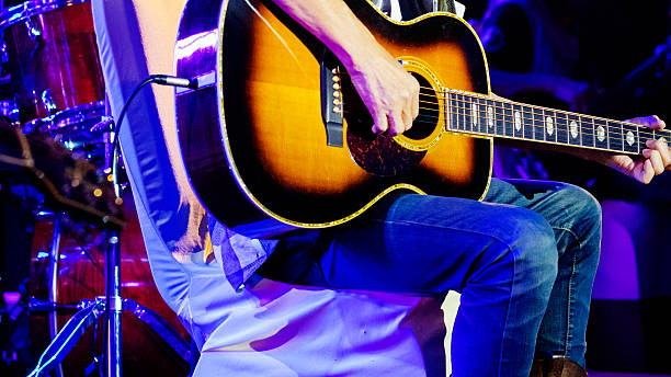 istock Sitting guitarist on stage and in light effects 2214377025