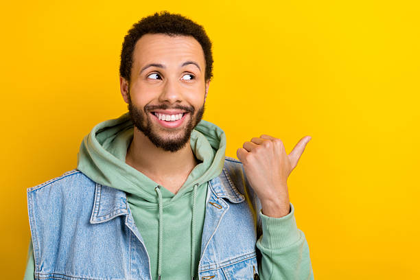 istock Portrait of positive handsome guy beaming smile look indicate thumb finger empty space isolated on yellow color background 2214377090