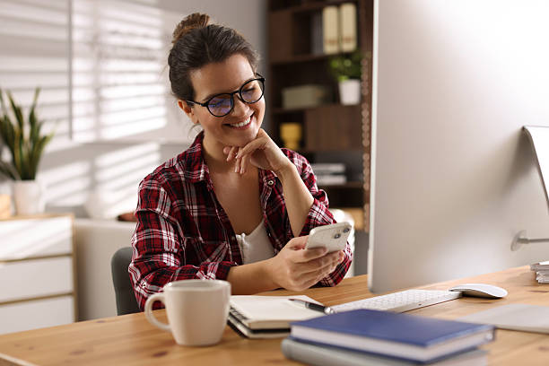 istock Happy woman using smartphone at desk with computer indoors. Home office 2214377200