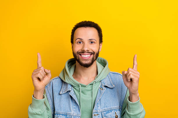 istock Portrait of nice attractive guy beaming smile direct fingers up empty space ad isolated on yellow color background 2214377280