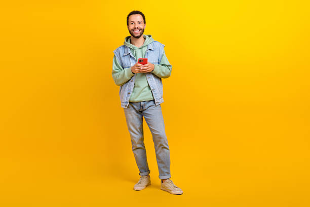 istock Full body size photo of funny young hispanic guy using smartphone gadget apple device modern technology isolated on yellow color background 2214380297