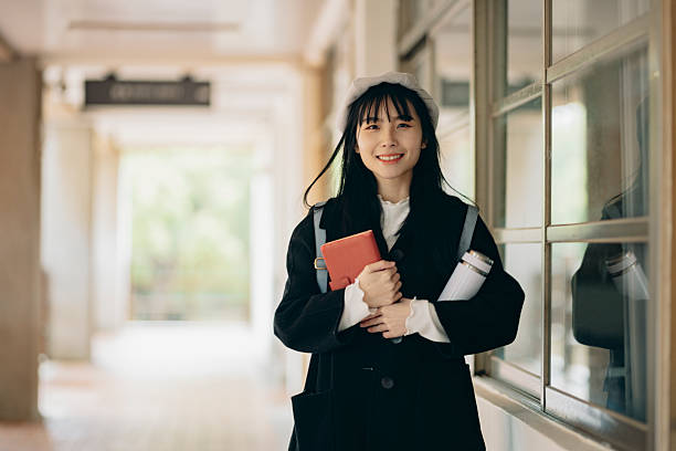 istock An Asian male student stands confidently on a university campus, wearing a backpack and smiling directly at the camera. 2214385769