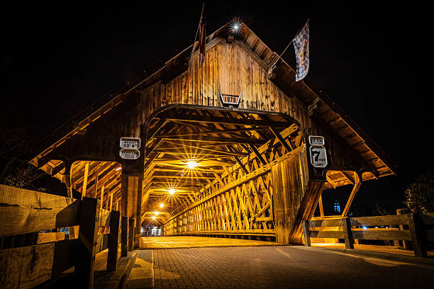 Photo of Bavarian Inn old wooden covered bridge in Frankenmuth Michigan illuminated at night with warm lights and Bavarian charm.
