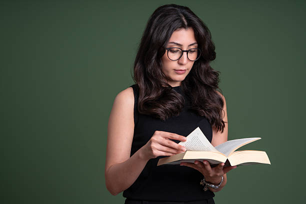 Young Woman Reading a Book Against Green Studio Background