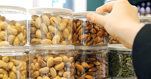 istock Customer's hand selecting a jar of almonds from a display of various nuts in transparent plastic jars, showcasing a variety of options for healthy snacking and ingredient shopping 2214395019