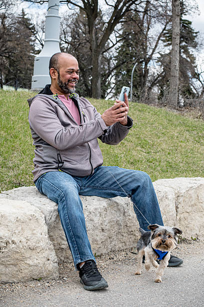 istock Caribbean Man Sitting with His Yorkshire Terrier and Smartphone 2214396477