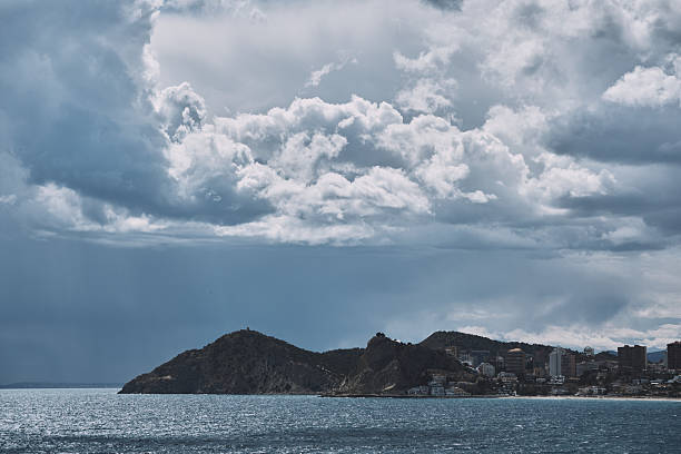 Dramatic coastal landscape with rolling clouds over coastal city and mountains.