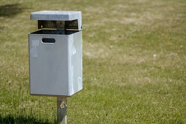 istock Metal trash can standing on green grass in a park 2214402724