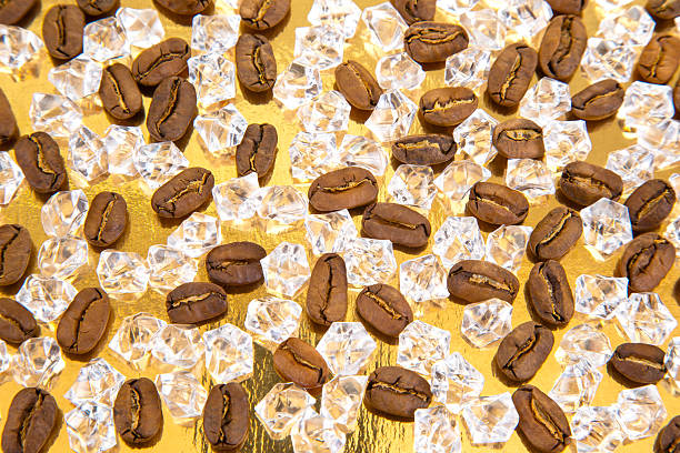 istock Roasted coffee beans scattered with ice cubes on a shiny golden surface, creating a cool yet warm aesthetic. Ideal for iced coffee ads, gourmet visuals, or refreshment concepts. 2214405420