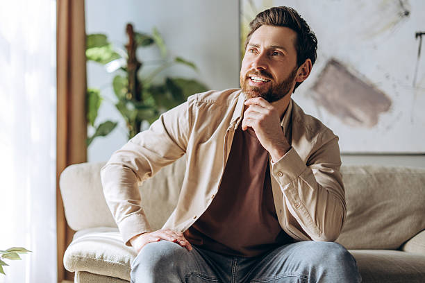 Happy middle aged Hispanic man smiling and thinking sitting on sofa at home