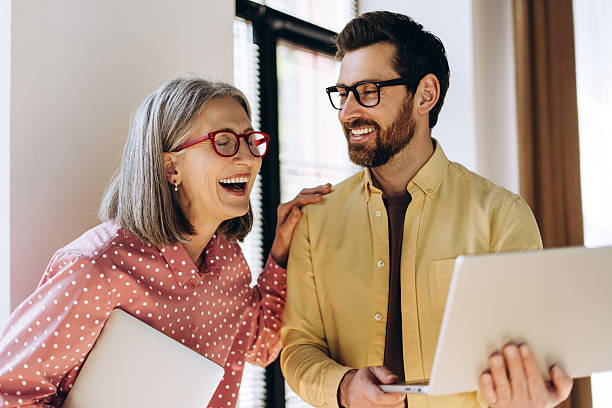 istock Coworkers laughing and using laptop in office: teamwork and success 2214412773