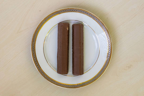 Two chocolate-coated water biscuits with chocolate cream sit on a white ceramic plate atop a wooden table. A delectable snack perfect for satisfying your sweet cravings. Top view.