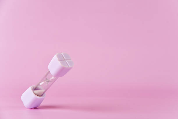 istock Little white hourglass falling on a soft pink backdrop 2214441331
