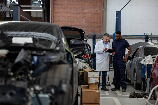 Senior mechanic talking to an employee at a car garage and using a digital tablet - vehicle breakdown service concepts