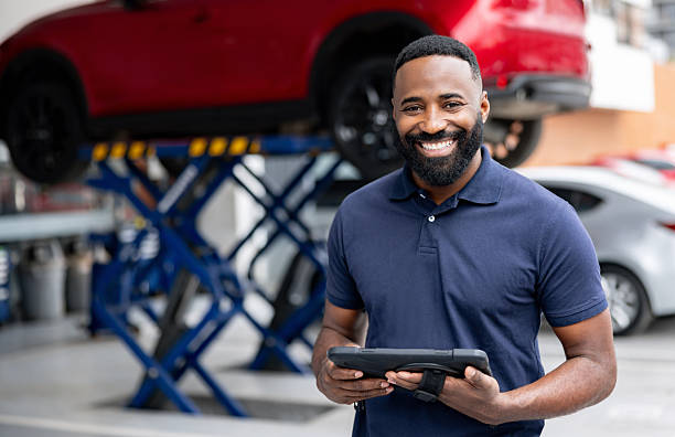 Portrait of an African American mechanic working at a car garage and holding a digital tablet while looking at the camera