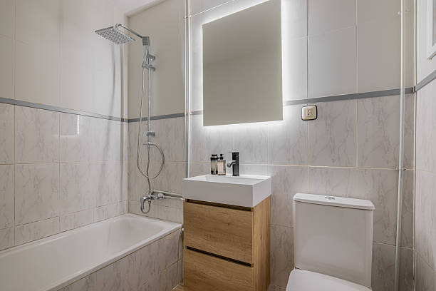 istock Bathroom with marble tile walls wood vanity white sink backlit mirror and overhead rain shower fixture 2214465044