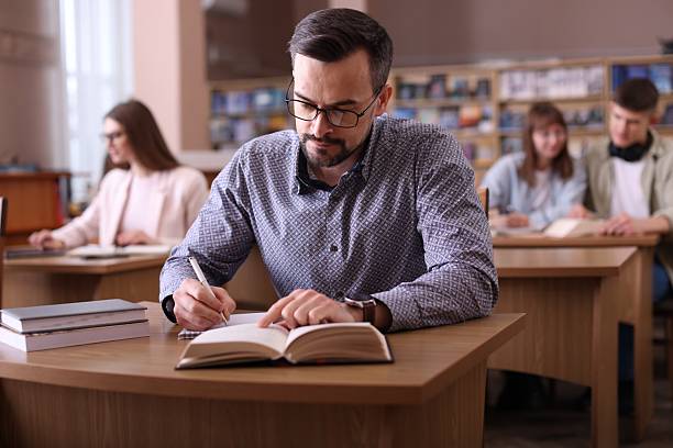 istock Handsome man reading book and taking notes at desk in public library 2214468258