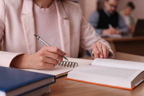 istock Woman reading book and taking notes at desk in library, closeup 2214468306