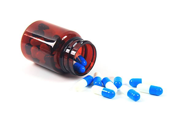 Close-Up Of Capsules Spilling From Bottle Against White Background