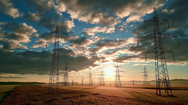 istock Power grid towers stand tall in a vast field under a cloudy sky. 2214484480