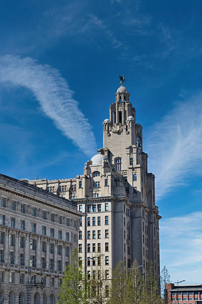 The image showcases the Liver Building under a blue sky with streaky clouds, alongside a smaller adjacent building in Liverpool, UK.