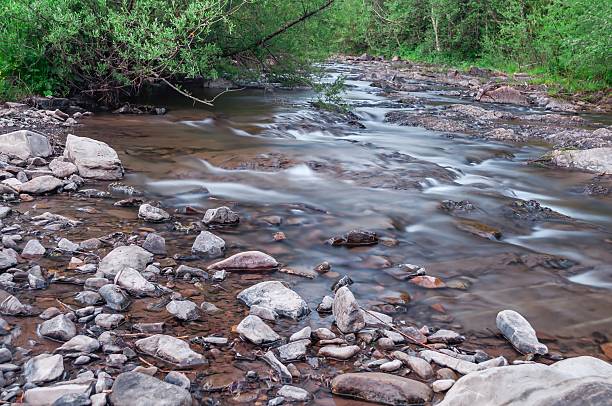 istock A tranquil river flows gently over smooth stones, captured with a long exposure for a dreamy effect. 2214486441