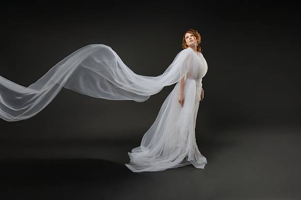 istock Elegant bride in flowing white gown with delicate veil in a dark setting 2214493771