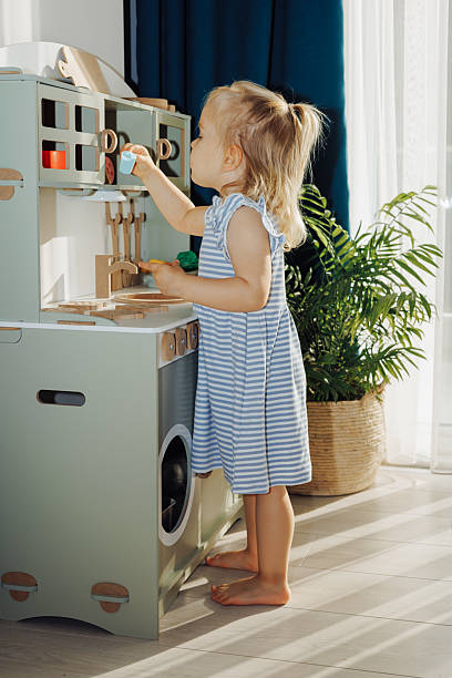 istock Child plays with kitchen toys while holding an apple in a bright, modern indoor play space 2214494801
