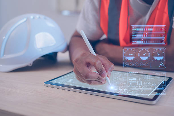 istock Engineering man wearing orange vest sitting in office hard hat on table using pen working on digital tablet analysing data charts on virtual screen 2214495303