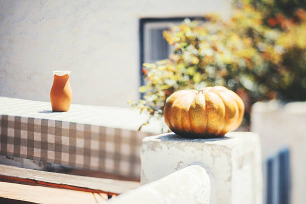 Bright outdoor still life with a rustic ceramic jug on a checkered table and a large pumpkin resting on a sunlit whitewashed wall, captured in soft focus with tilt-shift effect for dreamy atmosphere