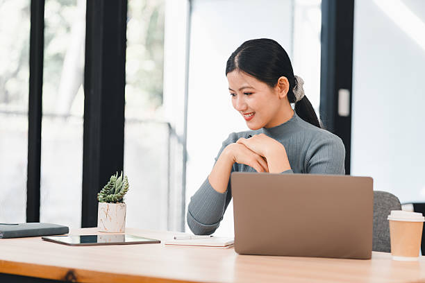 istock Woman smiling while working on laptop at modern office desk with small plant. 2214505601