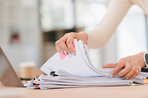 istock Person organizing stack of documents on desk, with laptop and coffee cup in background. 2214505764