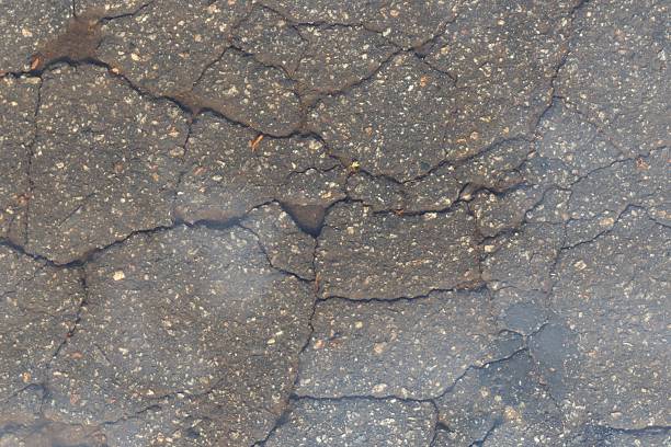 istock Cracked Asphalt Road Surface with Pebbles and Dust — Urban Texture Background 2214514728