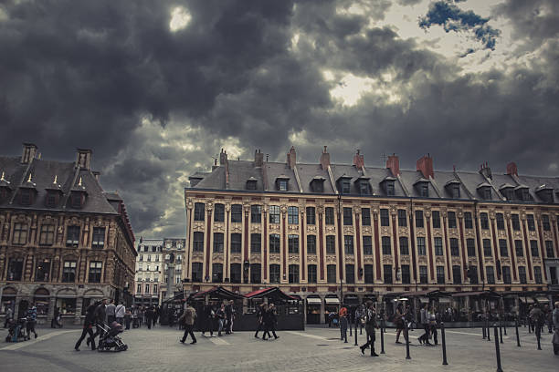 Lille, France - Rainy day view of the iconic red-brick Belfry of the Chambre de Commerce at the Grand Place area in Vieux Lille, with people walking under umbrellas, historic European architecture and reflections on the wet square. Lille Chamber of Commerce and Industry Nouvelle Bourse with bell tower on Place du Theatre square in historical city center