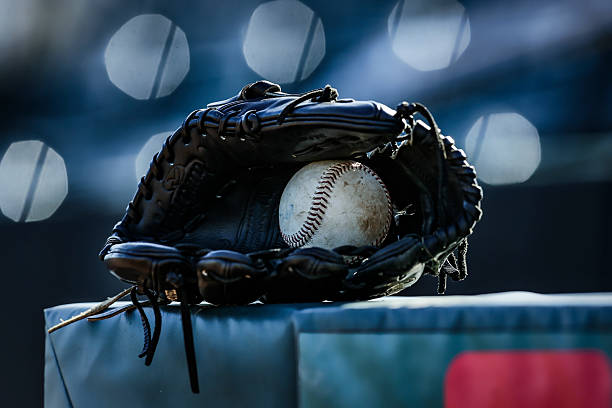 Baseball in a mitt at a low angle on a field with stripe and dramatic lighting and dark background