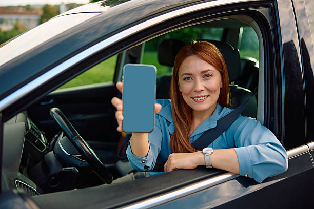 istock Happy woman holding smart phone with black screen while driving a car. 2214535406