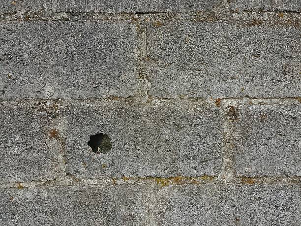 istock A slightly weathered grey concrete brick wall with a small hole or indent in the middle. 2214538617