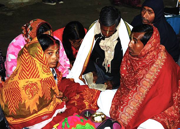 Family of Pilgrims sitting together by the banks of the Ganges river reading and reciting mantras and prayers from the sacred Hindu texts. These recitations are part of the spiritual activities and rituals performed during the holy festival of Kumbh Mela in the city of Prayagraj.