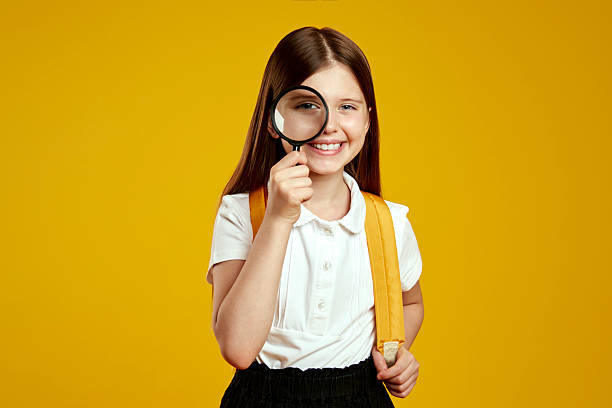 istock Curious young schoolgirl smiling confidently while holding magnifying glass against vibrant backdrop 2214548748