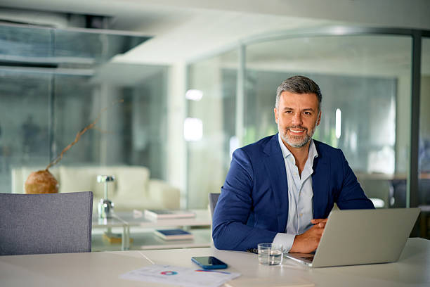 istock Confident businessman smiling at camera in modern office working on laptop 2214551536