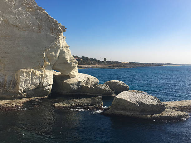 istock a white rock cliff by a blue sea with layered rock and soft waves meet shore. 2214552299