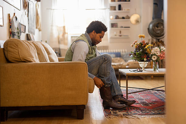istock Man putting on cowboy boots in living room 2214554059
