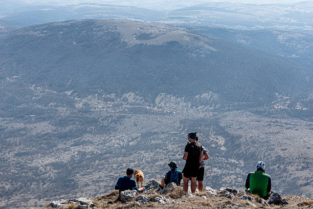 Group of hikers and their canine companion enjoying a well-deserved break on a mountain summit, soaking in the breathtaking views of the vast valley stretching below