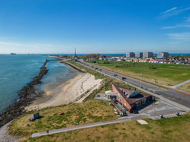istock A coastal view showing a quiet seaside town with a rocky shoreline, green open fields, a road with passing vehicles, and residential buildings in the distance under a clear blue sky. 2214560351