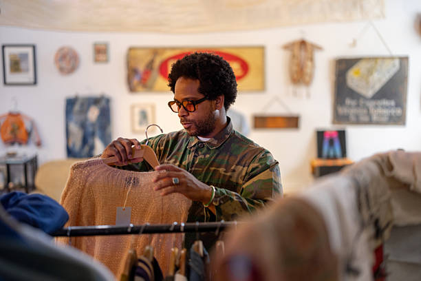 Man carefully selecting garments in a vintage second-hand shop, examining unique pieces and enjoying the charm of sustainable fashion