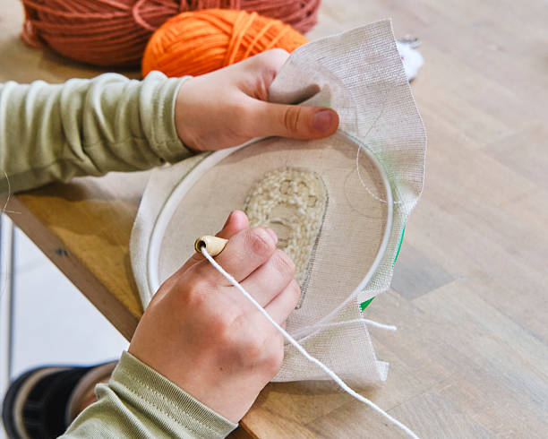 Close-up of child s hands using round hoop and punch needle for embroidery on fabric.