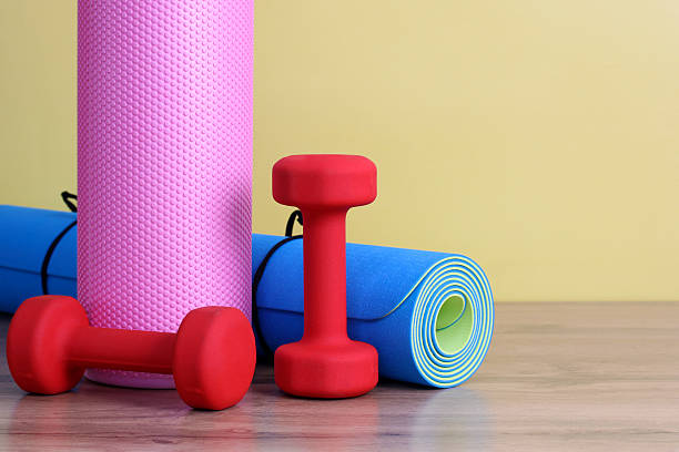 istock two red dumbbells, a yoga mat and a pink MFR massage roller on a yellow background. an empty space for your text on the right. 2214576028