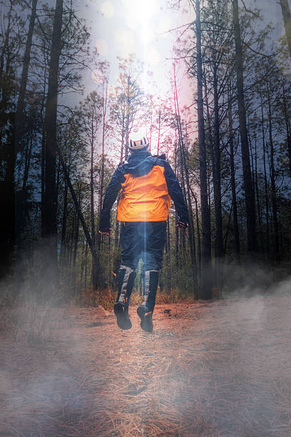 Hiker wearing an orange vest and helmet jumping on a forest path with light beams and fog