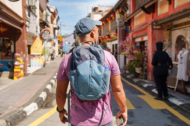 Man with blue backpack walking through a colorful street in George town, Penang, Malaysia on a sunny day.