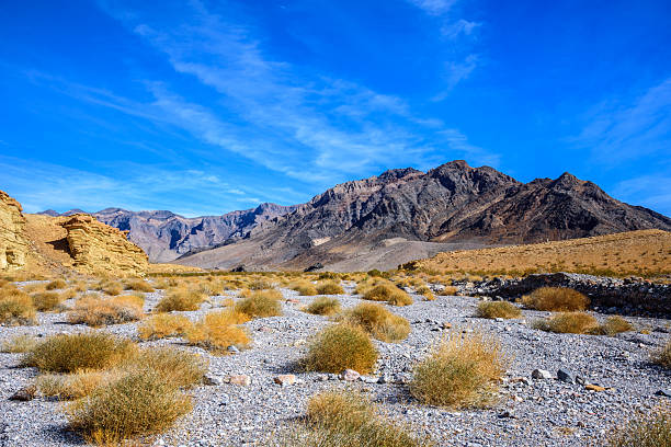 Looking across the entrance to Hole in the Wall Canyon, layers of golden sedimentary rock rise against the rugged peaks beyond. Shaped by ancient seas, earthquakes, and floods, this wild landscape reveals the raw geological history that makes Death Valley so extraordinary.  Hole in the Wall Canyon is in Death Valley National Park near Furnace Creek, California, USA.